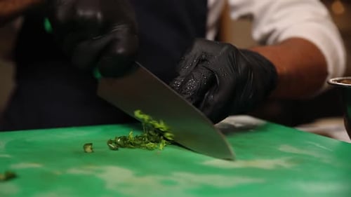 Gloved Chef Chopping Fresh Green Herbs
