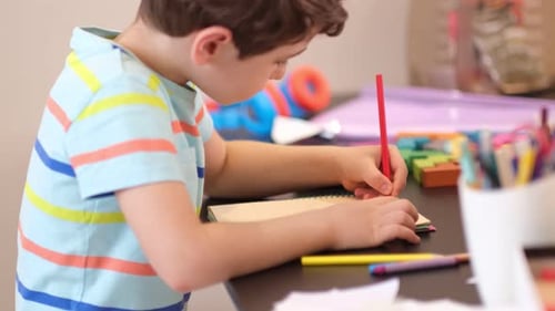 Child Drawing in Notebook with Colored Pencil