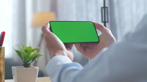 Close up of man's hands holding a mock up green screen smartphone on a desk