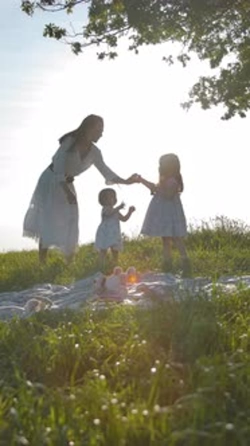 Vertical of Happy Family of Mom and Two Little Daughters are Resting in a Meadow Far From the City