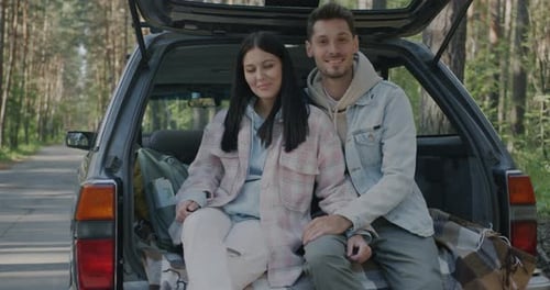 Portrait of Happy Young People Husband and Wife Sitting in Car Trunk Relaxing During Road Trip in