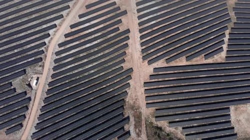 Blick von oben nach unten über einen riesigen Photovoltaik-Solarpark, Reihenpaneele, Hügel, sonnig