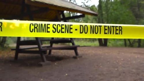 Police line crime scene tape in front of a camping area with sandy ground and fallen leaves, forest.