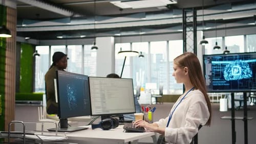 Woman Typing Code at Dual Monitor Computer in Office