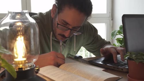 Close up of male studying and taking notes with laptop and books