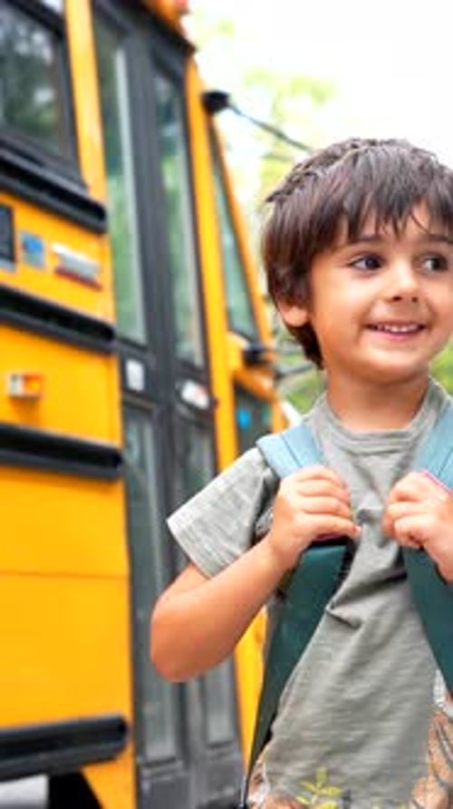 Happy pupil ready for school near yellow bus