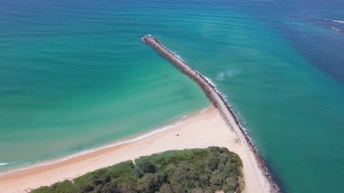 Breakwall se estende até o oceano calmo, Blacksmiths Beach ao meio-dia
