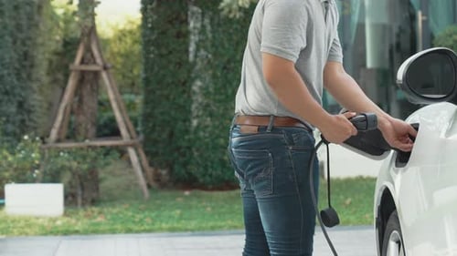 Progressive man unplugs the electric vehicle's charger at his residence.