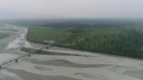 Wide river filled with muddy water after rains bordered by green landscape with meadow and forest
