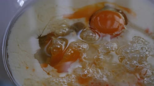 Slow motion pan around baking ingredients of egg, milk and oil in glass bowl with low depth of field