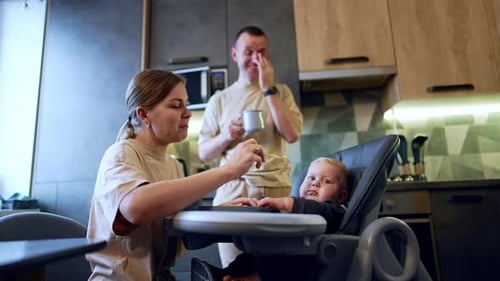 Woman Feeds Baby While Man Holds Coffee Mug
