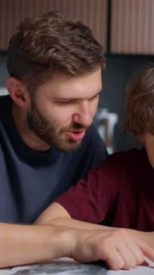 Adult Male Teaching Young Boy with Focused Expressions While Looking at and Discussing the Contents