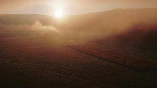 Aerial view of mystical orange fog over the meadow at sunset. Red mist over the peaceful landscape.