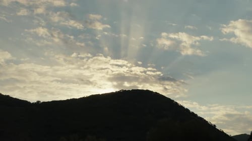Sonnenstrahlen scheinen über einem Silhouettenhügel mit goldenem Licht und Sonnenstrahlen in den Wolken