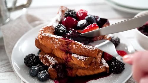 Eating Freshly Made French Toast Garnished with Mix Berry Compote and Powder Sugar