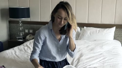 Young Businesswoman Talking on Cellphone and Eating Breakfast in Hotel 30s