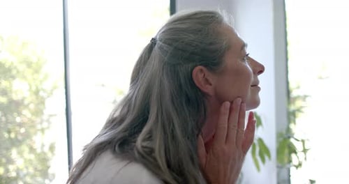 Senior Woman Gently Touches Face Indoors