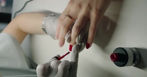 Manicure Master Hands in Gloves Applying Red Gel Polish on Client Nail