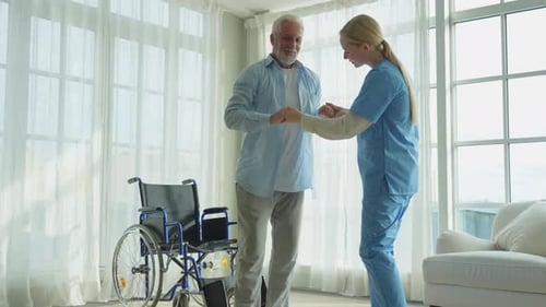 Rehabilitation Healthcare Physiotherapist Nurse Helps Old Man Patient in Wheelchair Stand Up Walking