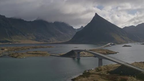 A car travels across a bridge connecting archipelago islands at the base of a steep mountain range d