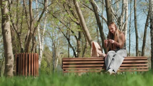 Girl knitting on bench in park on a sunny day