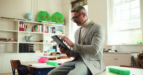 Teacher Using Tablet in Classroom Sitting on Desk