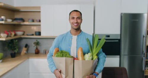 Smiling Man Holding Groceries in Bright Kitchen