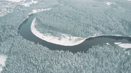 A serene aerial view of a snow-covered forest surrounding a winding river bend. The tranquil winter