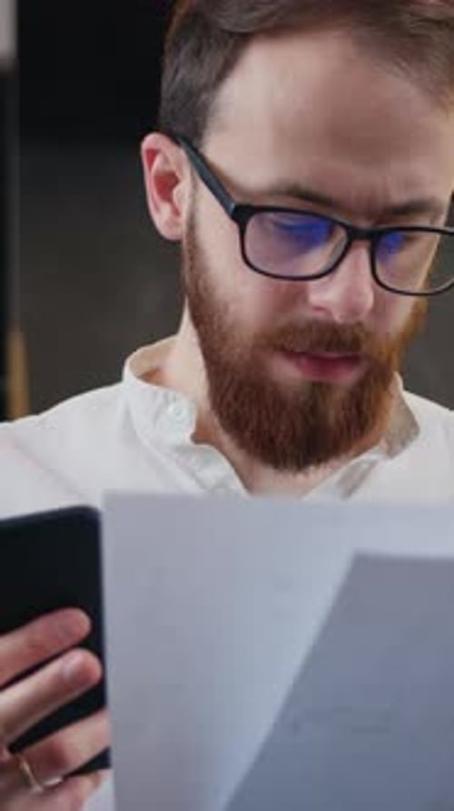 Man Reads Document and Uses Smartphone Indoors
