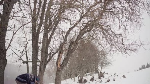 Man Cutting Tree Trunk With Chainsaw In The Forest In Winter - Wide Shot