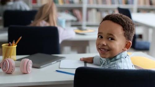 Smiling Boy Sits at Desk in Classroom