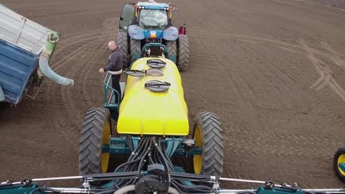 Blue tractor with yellow seeder working on the field in Ukraine OA
