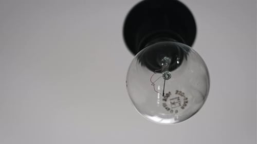 Hanging on Wire Incandescent Bulb Turns On and Off Flickers on White Background