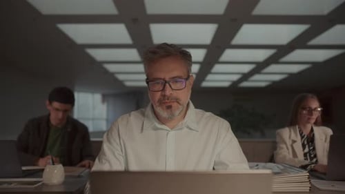 Homem focado trabalhando no laptop na mesa com a equipe de negócios ao redor