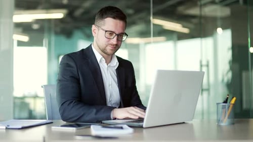 Busy businessman in a formal suit typing on a laptop while sitting at a workplace in business office
