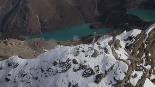 Aerial top down shot of summit cross on snowy peak with mountain lake in the valley during sunny day