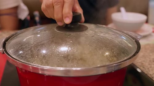 Opening a hotpot filled with bubbling boiling broth stock for a mixed vegetable and meat soup, insid