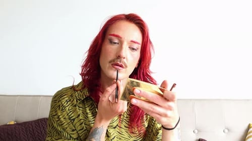 Young non-binary person applying lipstick on white background