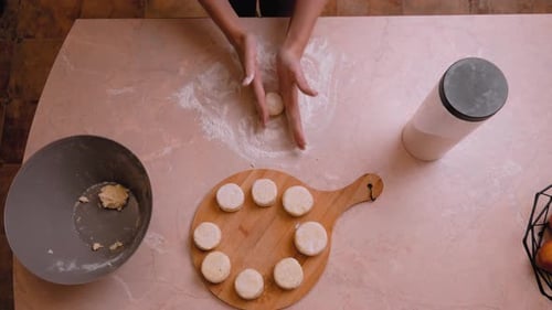 Closeup of hands dusting flour and shaping dough into small buns on work surface