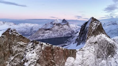 Cinematic aerial view of Segla peak on Senja Island, Norway, steep snow-covered cliffs above icy