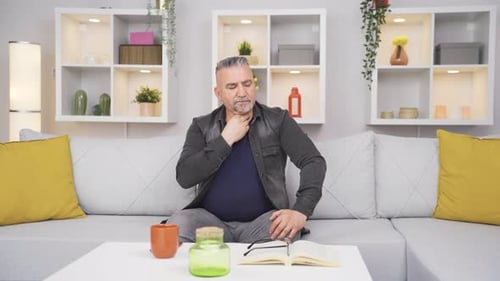 Adult Man Touches Neck While Seated on Sofa