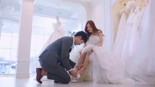 Asian beautiful bride trying on wedding shoes with her fiance in studio.