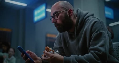 Boarding Lounge of Airline Hub at Night Man Eating Burger and Scrolling Smartphone