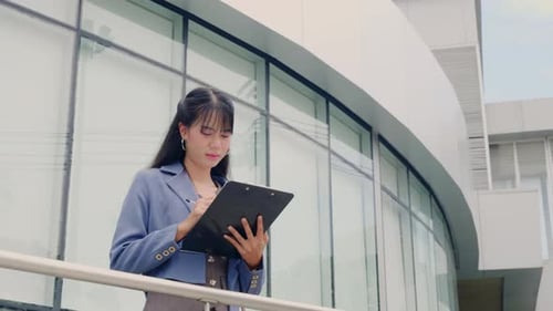 Young Businesswoman Diligently Works Outdoors Completing Tasks on Clipboard Standing Near Modern