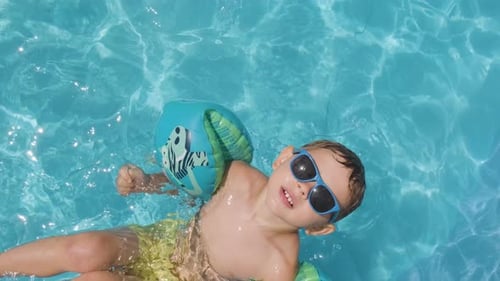 Garoto legal olhando para a câmera, usando óculos escuros e carros alegóricos. Piscina de água cristalina, Topdown