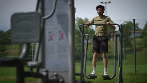 A Man is Engaged in Exercising on the Outdoor Gym Equipment Located Within a Parks Vicinity
