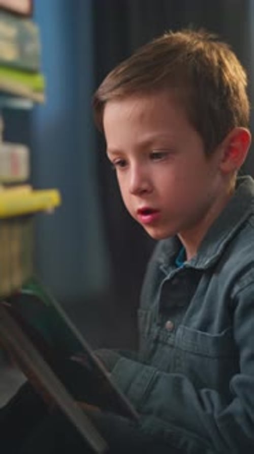 Focused Boy Reading Book by Bookshelf