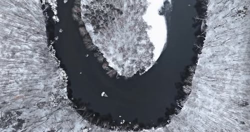 Top down view of frozen river and snowy winter forest.