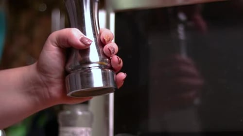 A close up of a young lady using a salt grinder to add some salt on the prepared food.