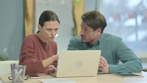 Professionals Reviewing Laptop in Bright Office Setting